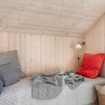 Ein Bett mit Kissen und Decke in einem Holzraum mit Wandlampe.