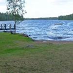 Seeufer mit Holzsteg und grünem Rasenbereich.