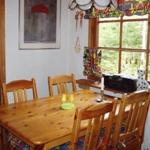 Holztisch mit Stühlen, Fenster mit bunten Vorhängen und Wandbild.