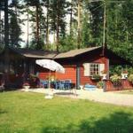 Rotes Holzhaus mit Garten, Terrasse und Sonnenschirm in Waldnähe.