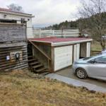 Hinterhof mit Carport, Ladestation und Holzterrasse. Ein Auto steht bereit.