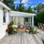 Terrasse mit Grill, Blumen und Glasveranda im Hintergrund.