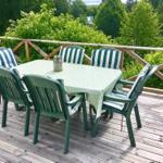 Terrasse mit Tisch und sechs Stühlen, umgeben von grüner Vegetation.