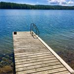 Holzsteg mit Leiter führt ins klare Wasser eines Sees.
