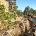 Person steht auf Felsen am Ufer mit Bäumen und klarem Himmel.