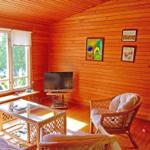 Wohnzimmer mit Holzwand, Fernseher, Sessel und Glas-Tisch. Fenster mit Blick auf Balkon.