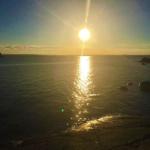 Sonnenuntergang über dem Wasser mit Felsen und Bäumen am Ufer.