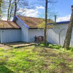 Haus mit Holzterrasse, umgeben von Bäumen und Grasflächen.