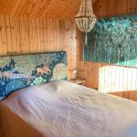 Schlafzimmer mit Holzwänden, Bett mit Tiermotivkopfteil und Wandbild mit Pfauenfedern.