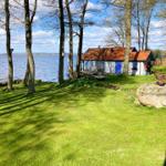 Haus mit Terrasse am See, umgeben von Bäumen und Gras.