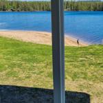 Blick auf einen See mit Sandstrand und Wald im Hintergrund durch eine Glasschiebetür.