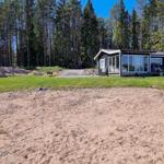 Zwei Häuser mit Terrassen stehen auf grünem Grundstück vor einem Wald.