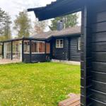 Schwarze Holzhütte mit Glasveranda und grünem Rasen im Wald