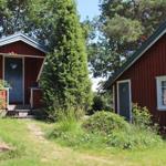 Zwei rote Holzhäuser mit weißen Fensterrahmen stehen im Gras zwischen Bäumen.