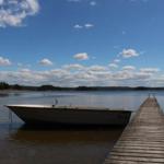 Ein kleines Boot liegt am Steg eines Sees mit bewölktem Himmel.