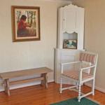 Raum mit Holzboden, Stuhl und Bank. Wandbild und weißer Schrank sind sichtbar.