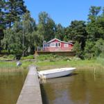 Rotes Haus am See mit Bootssteg und weißen Boot.