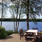 Terrasse mit Tisch und Stühlen am See. Blick auf Wasser und Bäume.