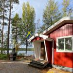 Rotes Holzhaus mit Schwedenflagge, Grill und Seeblick.