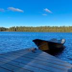 Ein kleines Boot liegt am Holzsteg eines Sees mit Wald im Hintergrund.