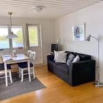 Wohn- und Essbereich mit Sofa, Tisch und Blick auf Wasser.