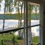 Blick auf ruhigen See mit Bootssteg und Birken durch große Fenster.