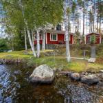 Rotes Holzhaus am See mit Bäumen und Steinen