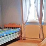 Zwei Betten mit bunten Bettwäschen, Fenster mit Vorhängen und Heizkörper.