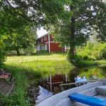 Rotes Haus mit grünem Garten und Wasserreflexion. Boot im Vordergrund.