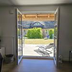 Durch offene Türen Blick auf Terrasse mit Liegen und grünen Hecken.