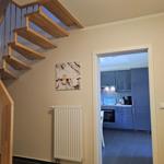 Holztreppe führt zur oberen Etage. Küche mit blauen Schränken ist sichtbar.