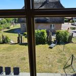 Von innen betrachtet: Garten mit Liegestuhl und Blick auf ein Haus mit Strohdach.