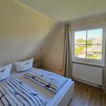 Doppelbett mit Vogelmotiv, Fenster mit Blick auf Dächer und Bäume, Holzboden, weißer Schrank und Heizkörper.