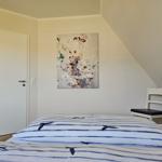 Schlafzimmer mit Bett, Stuhl und Wandbild unter Dachschrägen.