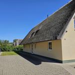 Ferienhaus mit strohgedecktem Dach und gepflastertem Vorplatz.