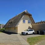 Haus mit Strohdach, gepflasterter Hof und parkender weiße Auto.