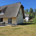 Haus mit Strohdach, Terrasse mit Tisch und Stühlen, Garten und Liegestuhl.