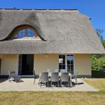 Haus mit Strohdach, Terrasse mit Tisch und Stühlen, Garten und Sitzgelegenheiten.
