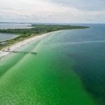 Aerial view of a long beach with clear water and a pier.