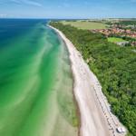 Strand mit kristallklarem Wasser und grüner Landschaft neben einem Dorf.
