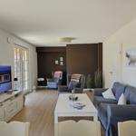 Wohnzimmer mit Sofa, Sesseln und Fernseher. Holzfußboden und große Fenster.