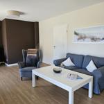 Wohnzimmer mit Sofa, zwei Sesseln, Tisch und Wandbild.