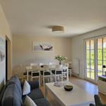 Wohn- und Essbereich mit Sofa, Tisch und Stühlen, Fernseher und Blick auf Garten.