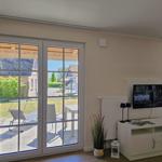 Wohnzimmer mit TV und Blick auf Terrasse mit Garten.