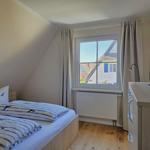 Schlafzimmer mit Bett, Fenster und Schrank. Blick auf Dachhäuser.