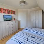 Schlafzimmer mit Bett, Kleiderschrank und TV. Wandbild und Holzboden.