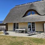 Haus mit Strohdach, Terrasse mit Tisch, Stühlen und Liegestühlen.