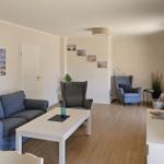 Wohnzimmer mit Sofa, Sessel und Fernseher an der Wand