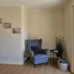 Ein Raum mit grauem Sessel, Pflanzen und Wandbildern an der Wand.