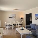 Wohn- und Essbereich mit Sofa, Tisch und Stühlen. Wandbilder zeigen Strand.
